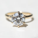A classic solitaire engagement ring featuring a round brilliant-cut clear diamond in a six-prong setting on a polished yellow gold band, photographed on a clean white surface.