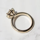 A gold ring with a large clear diamond in a six-prong setting, photographed on a white marble surface.
