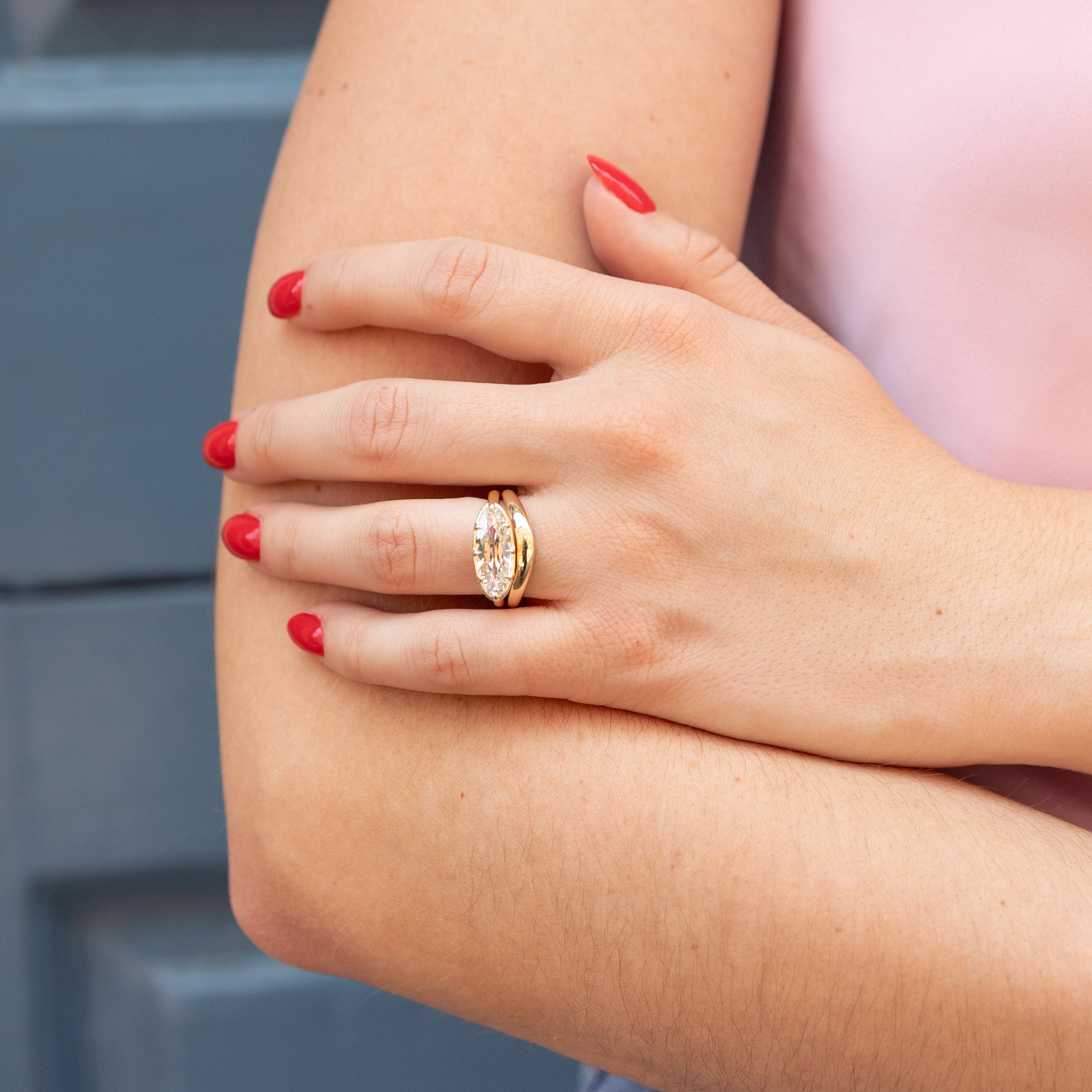A close-up lifestyle shot of a person's hand resting on their arm, showcasing a gold ring with a moval-cut diamond. The ring features a yellow gold band with a georgian setting.