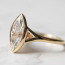 A macro shot of the split shank on an engagement ring. The ring has a bezel set marquise in the center on a yellow gold band.