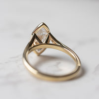 A view of the back of an engagement ring. The ring is yellow gold and cathedral set with a large marquise cut diamond.