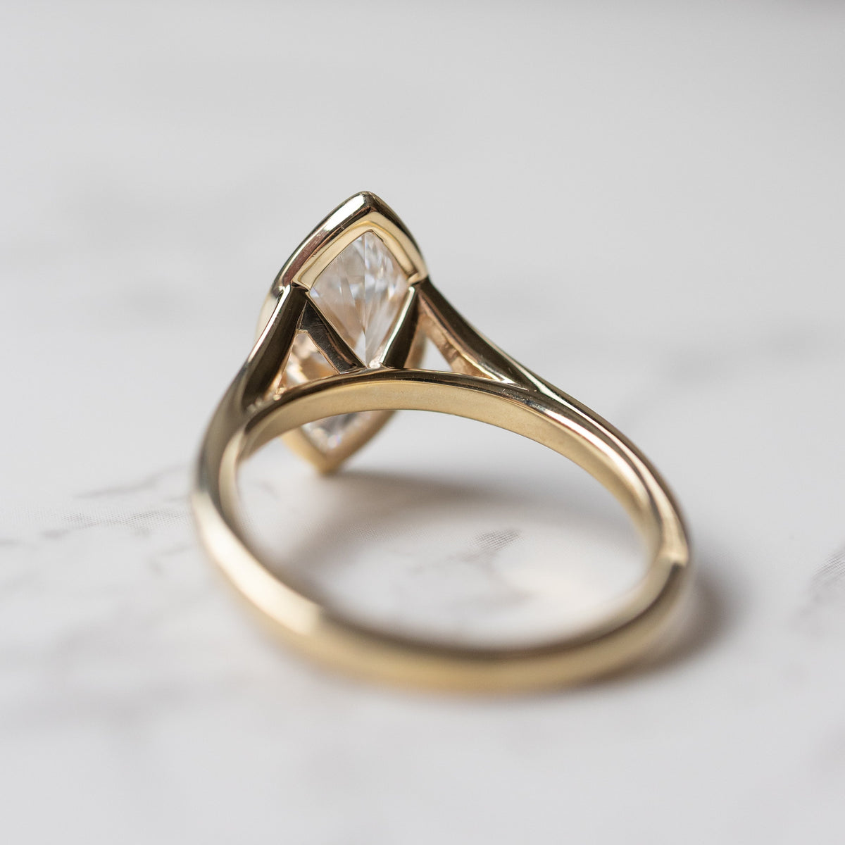 A view of the back of an engagement ring. The ring is yellow gold and cathedral set with a large marquise cut diamond.