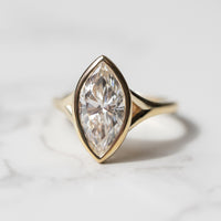 The front view of a split shank bezel engagement ring. The ring has a large marquise in the center and is set in yellow gold.