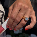 A large chunky gold cushion cut engagement ring setting on a ring finger