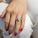 A close-up of a hand wearing a yellow gold ring set with a large radiant-cut diamond center stone, paired with a matching emerald-cut diamond band, against a soft white background.