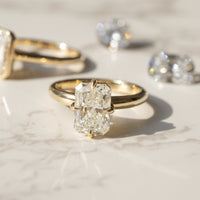 Two gold engagement rings with loose diamonds behind them arranged on a light marble surface in bright sunlight.
