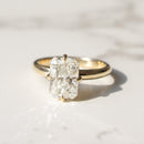 A yellow gold ring with a large rectangular radiant-cut diamond solitaire, resting on a white marble surface with soft shadows.