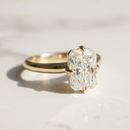 A yellow gold ring with a large rectangular radiant-cut diamond solitaire, resting on a light marble surface with a soft shadow.