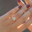 Two hands with red nail polish being held up against a blurry dark background. On the hand in the front is a large cushion cut diamond set in yellow gold.