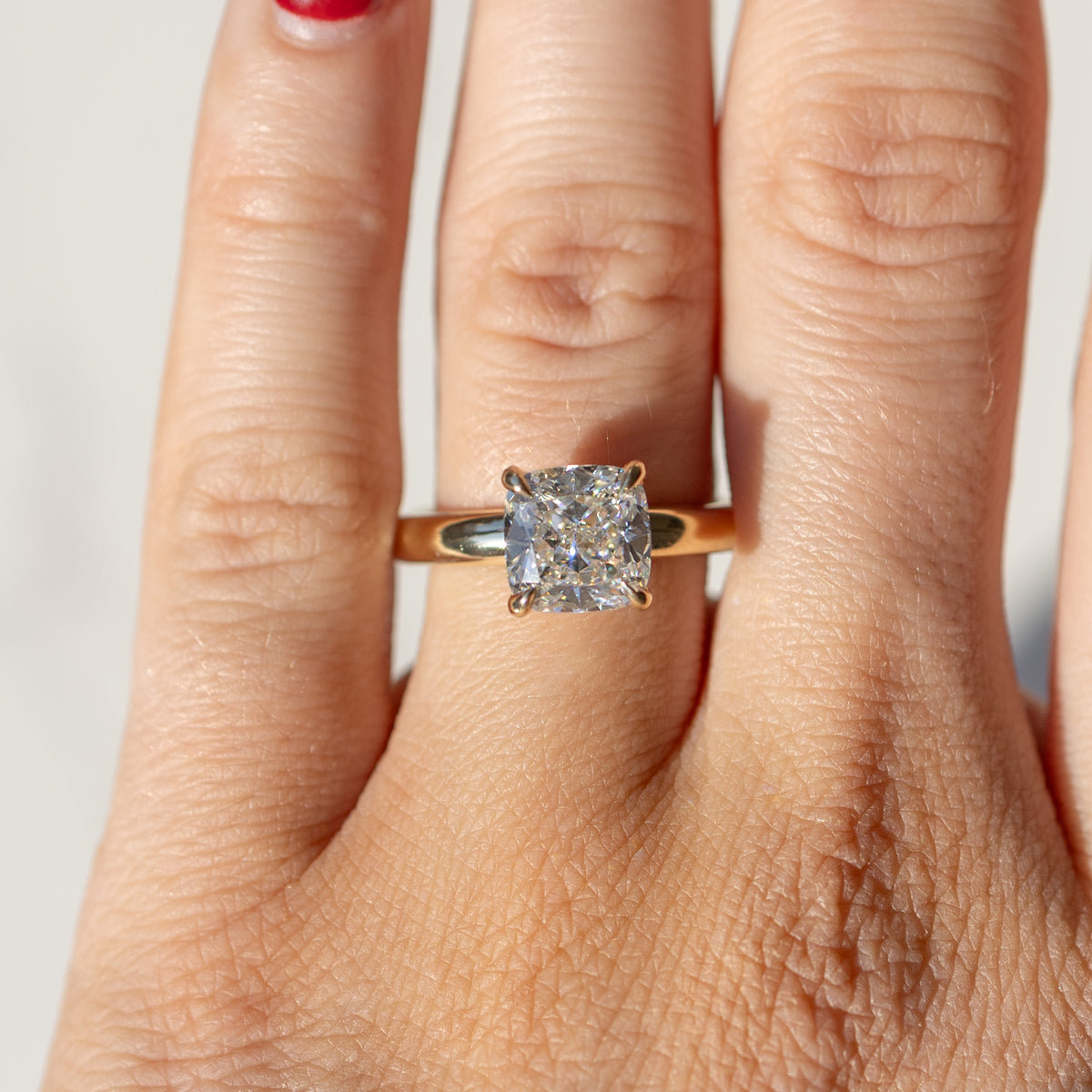 An on-hand shot of a large cushion cut engagement ring set in yellow gold sitting on the left ring finger of a hand.