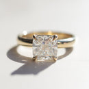 A yellow gold cushion cut engagement ring sitting on a white marble backdrop with sharp shadows.