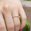 A hand against the side of a wooden bench. On the left ring finger of the hand is a yellow gold wedding band with stationed round diamonds.