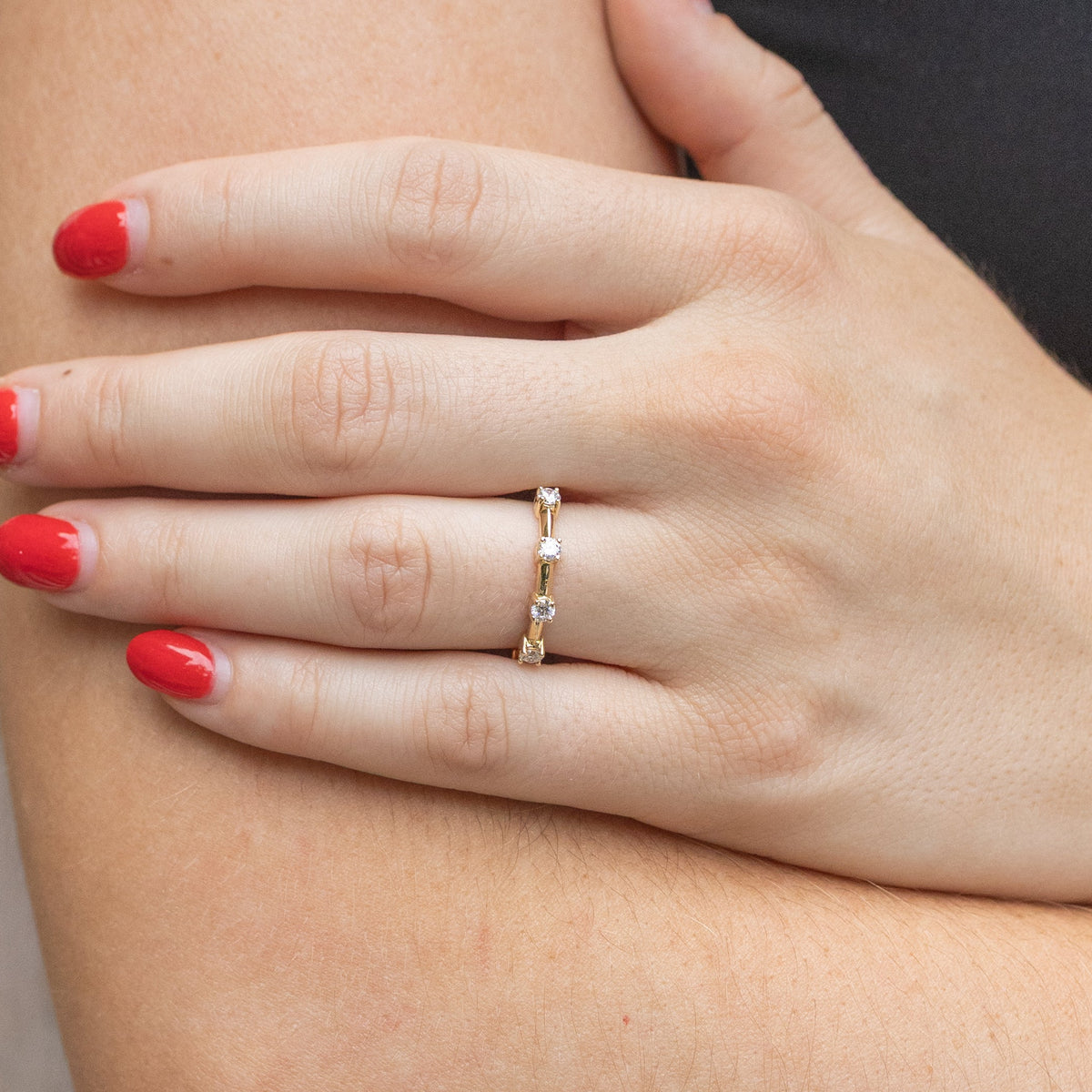 A woman resting her hand along her other arm at the elbow. On her left ring finger is a gold wedding band with spaced out round diamonds.