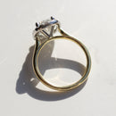 The side profile view of a dual-tone engagement ring with a yellow gold band and platinum basket. The ring is on a white marble backdrop.