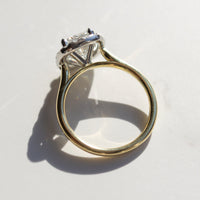The side profile view of a dual-tone engagement ring with a yellow gold band and platinum basket. The ring is on a white marble backdrop.