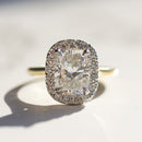 A large elongated cushion diamond engagement ring surrounded by a halo of round diamonds sitting on a white marble backdrop. The ring is yellow gold and platinum.
