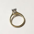 A gold engagement ring with a diamond in a silver and gold-colored setting, photographed on a light marble surface.