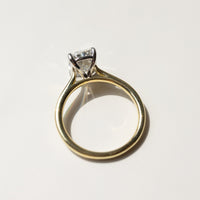 A gold engagement ring with a diamond in a silver and gold-colored setting, photographed on a light marble surface.