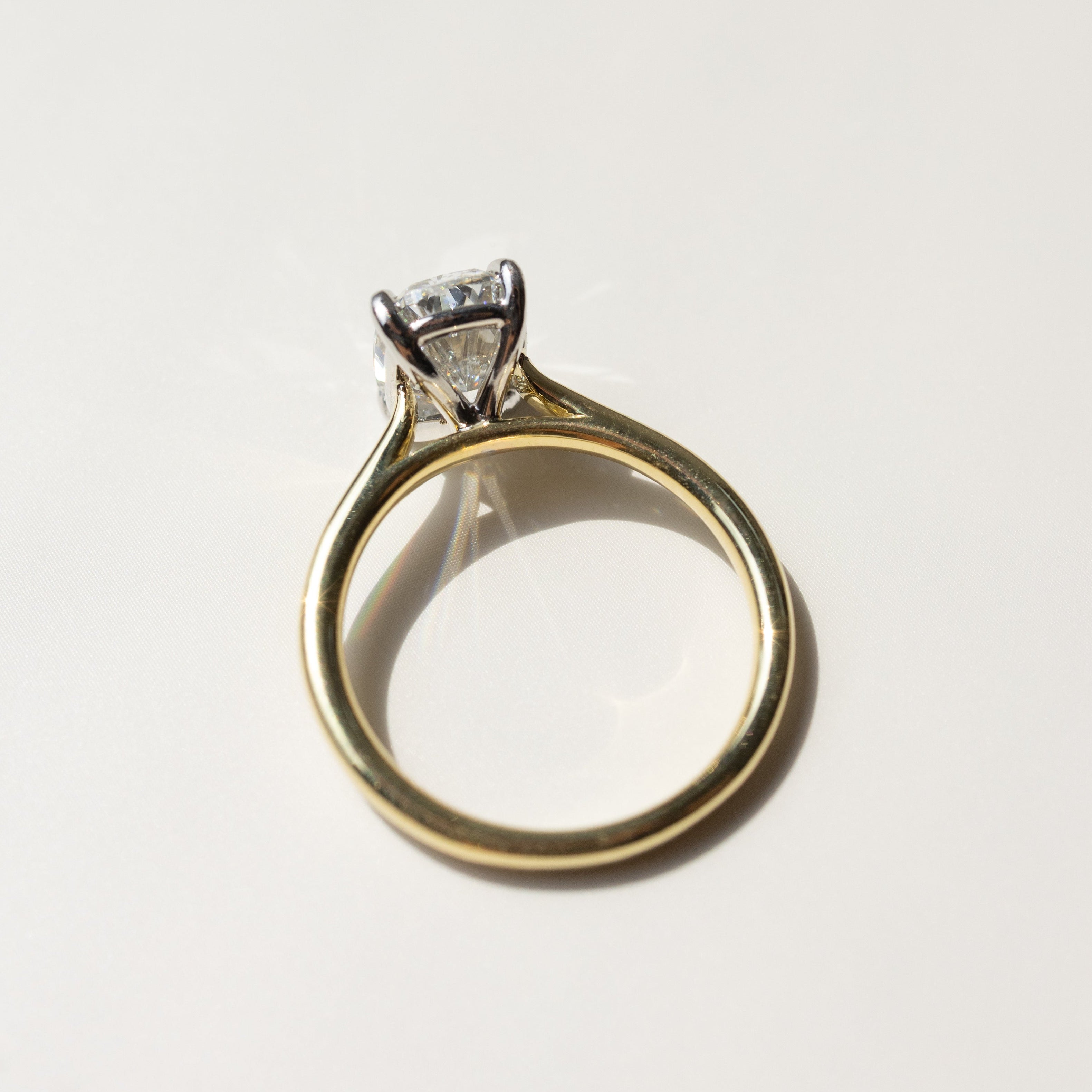 A gold engagement ring with a diamond in a silver and gold-colored setting, photographed on a light marble surface.