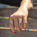 A close-up of a hand wearing a yellow gold ring stack with a large rectangular emerald-cut diamond, resting on a wooden bench.
