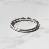 The back profile of a white gold diamond wedding band sitting on a white marble backdrop.