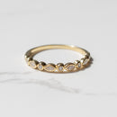 A dainty bezel-set yellow gold wedding band on a marble backdrop. The ring has alternating marquise and round diamonds.