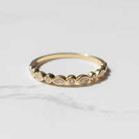 A dainty bezel-set yellow gold wedding band on a marble backdrop. The ring has alternating marquise and round diamonds.