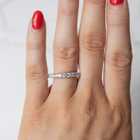 An on hand shot of a chunky diamond wedding band with a shared prong setting. The hand has red fingernail polish.