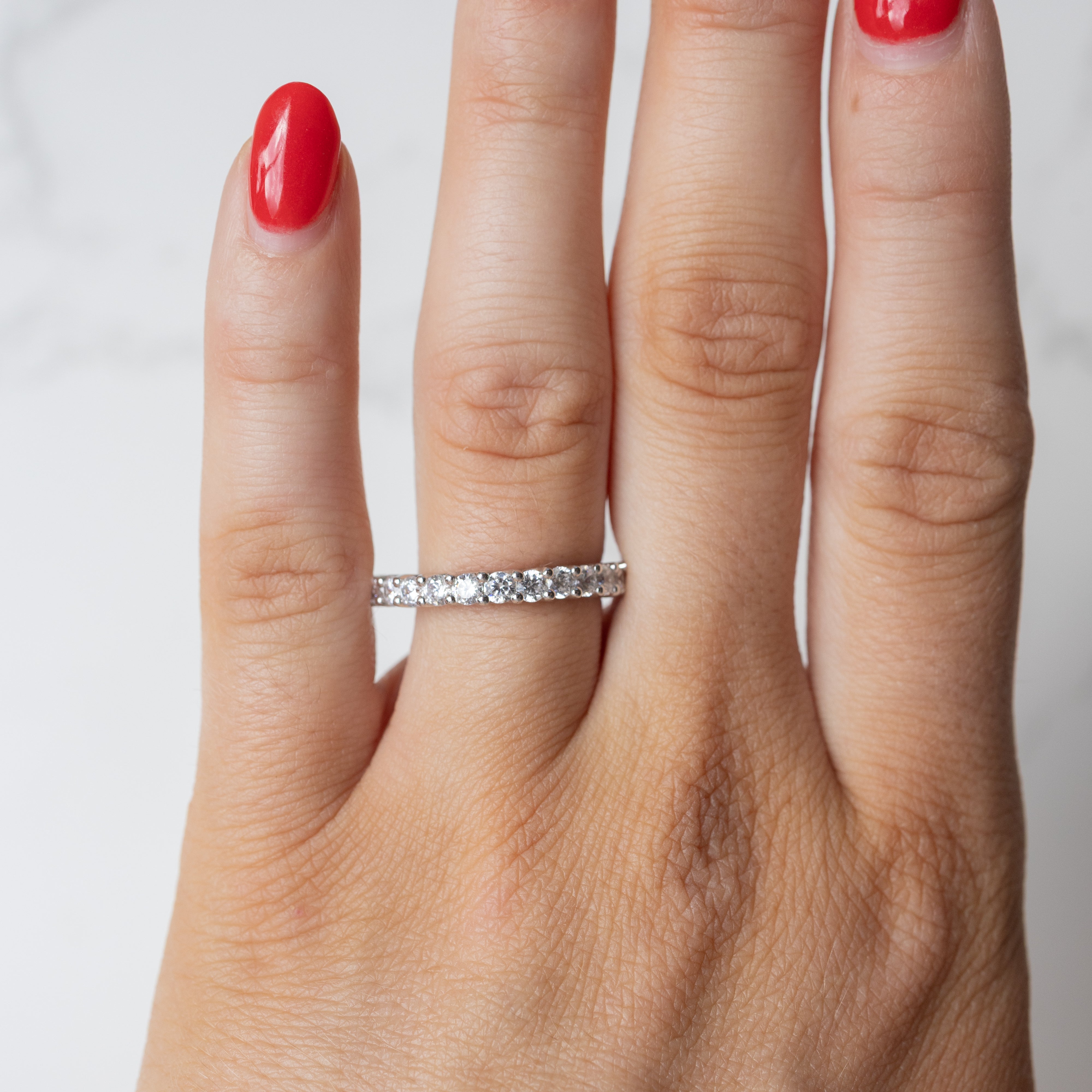 An on hand shot of a chunky diamond wedding band with a shared prong setting. The hand has red fingernail polish.