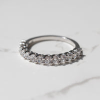A chunky diamond wedding band with scallop prong detailing sitting on a white marble backdrop.