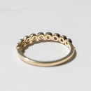 The back profile of a ring. It's a wedding band with small round bezel-set diamonds sitting on a white shadowy backdrop.