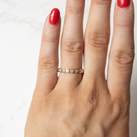 On hand shot of a yellow gold bezel-set wedding band with small round diamonds. The hand has red fingernail polish.