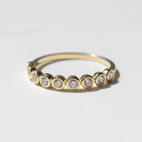 A yellow gold wedding band with small round diamond halfway down the band sitting on a white shadowy backdrop