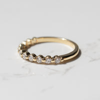 The side view of a yellow gold diamond wedding band with a row of small round diamonds sitting on a white marble backdrop.
