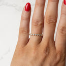 A close-up of a hand wearing a delicate gold eternity ring set with small round diamonds, shown against a light marble background.