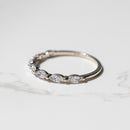 A dainty white gold diamond wedding band sitting on a white marble backdrop. The ring as a row of marquise diamonds with a shared single prong between them.