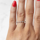 A close-up of a hand wearing a delicate silver band ring with a row of small marquise-cut diamonds, set against a light marble background.