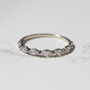 A white gold band ring featuring a row of marquise-cut diamonds, photographed on a light gray marble surface.