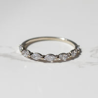A white gold band ring featuring a row of marquise-cut diamonds, photographed on a light gray marble surface.