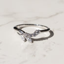 A silver ring featuring a curved, leaf-like cluster of clear marquise and round gemstones, resting on a light marble surface.