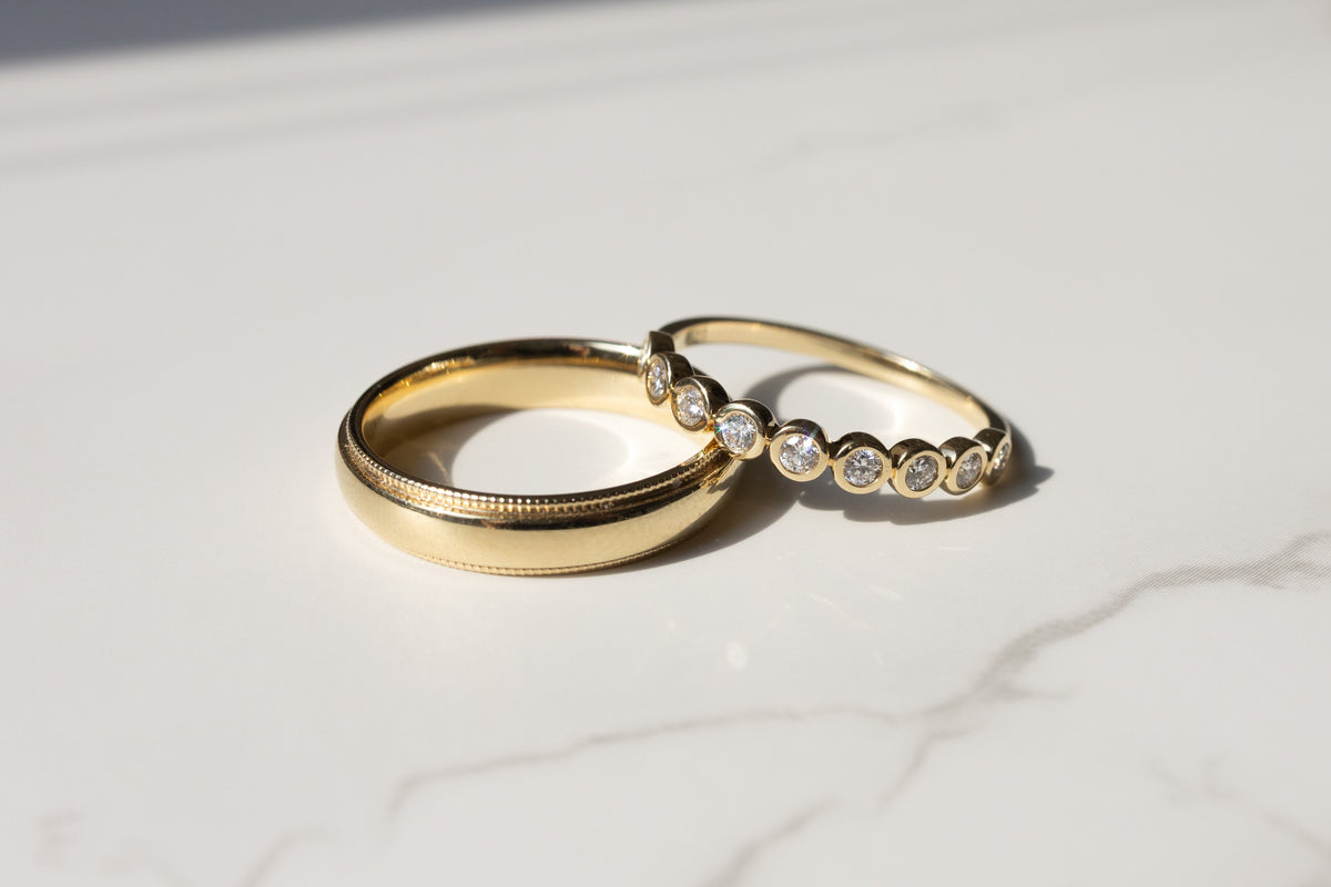 Two gold rings on a white marble surface, one plain and one with a row of small round diamonds.