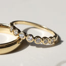 A close up of a gold round diamond bezel wedding band on a soft white marble backdrop with shadows