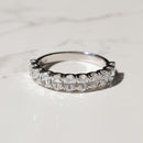 A platinum diamond band with large oval diamonds set halfway down the band on a white marble backdrop with shadows