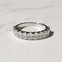 A platinum diamond band with large oval diamonds set halfway down the band on a white marble backdrop with shadows