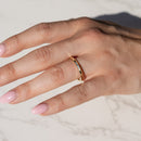 A close-up of a hand wearing a slim gold band ring with a knife edge point along the outer edge, resting on a light marble surface.