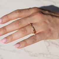 A close-up of a hand wearing a slim gold band ring with a knife edge point along the outer edge, resting on a light marble surface.