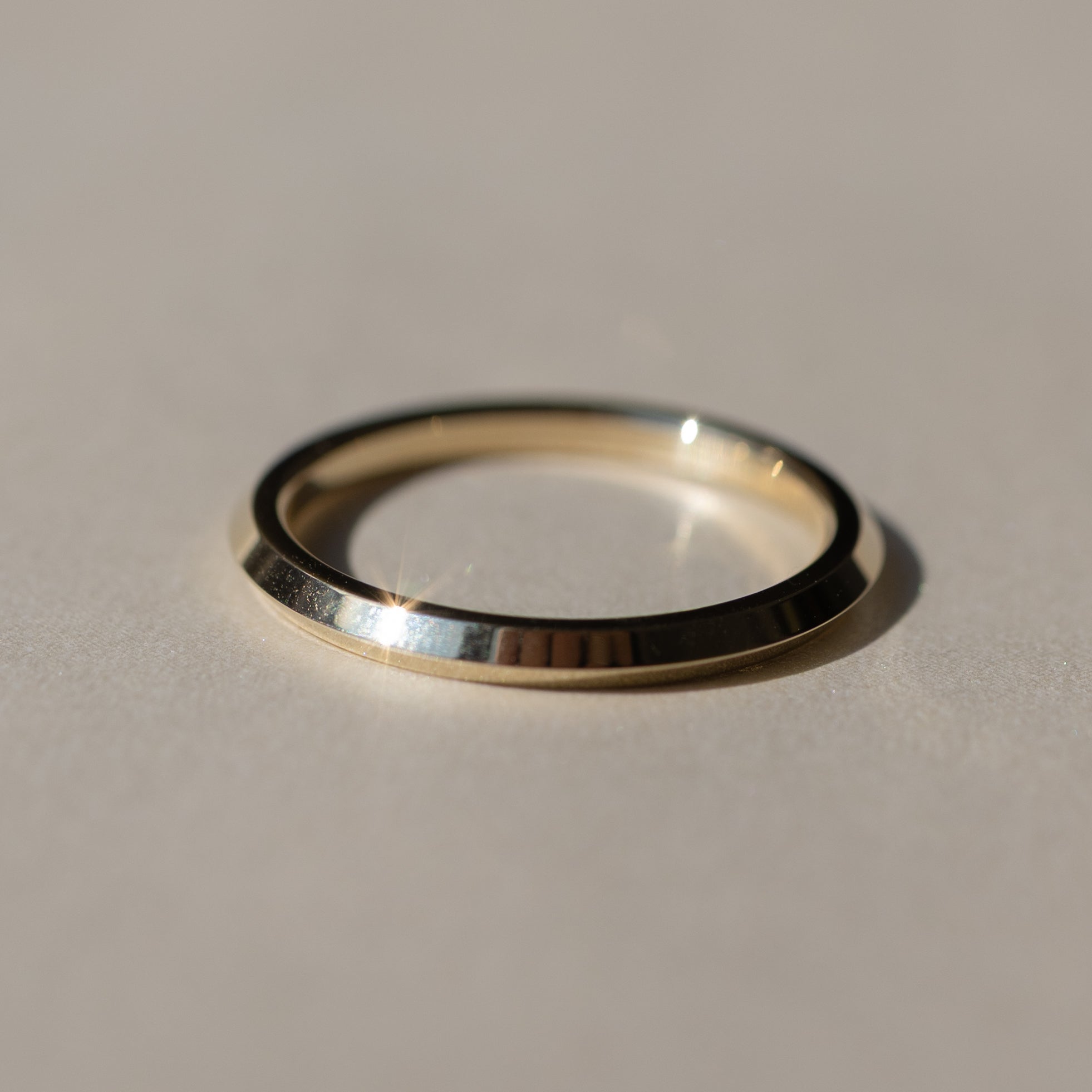 A minimalist polished metal ring, with a knife edge point in the middle of the band, resting on a neutral beige surface with a soft shadow.