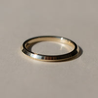 A minimalist polished metal ring, with a knife edge point in the middle of the band, resting on a neutral beige surface with a soft shadow.