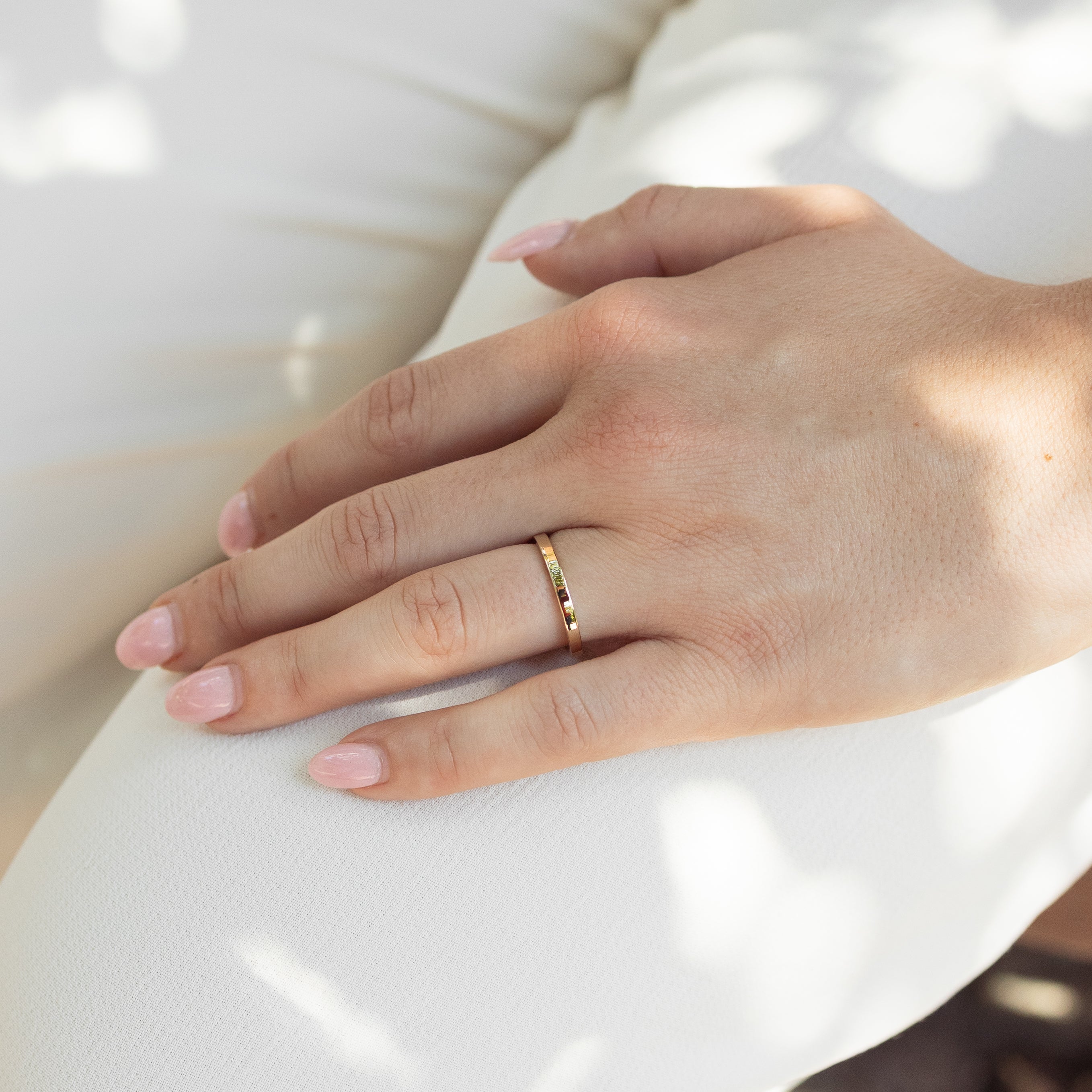 A close-up of a person's hand resting on white fabric, wearing a thin gold band ring.