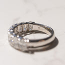 A diamond ring with oval-cut diamonds, shown in a close-up side view on a light marble surface. The inside of the band is stamped with 'LG'.